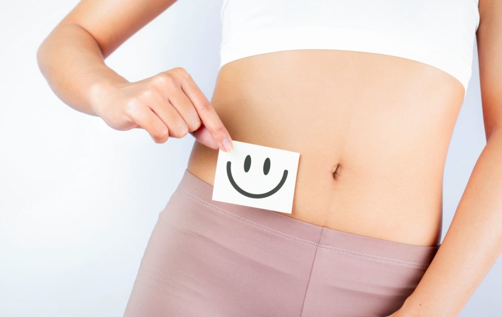 donna che tiene un foglietto di carta con una faccina sorridente all'altezza dell'intestino