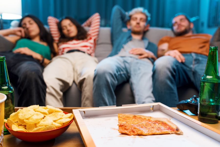 quattro persone distese sul divano dopo aver mangiato pizza e patatine fritte