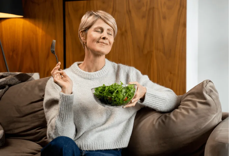 donna mangia una scodella d'insalata in divano