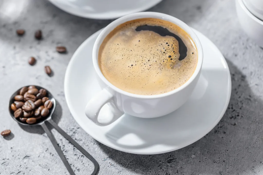 Tazza di caffè inquadrata dall'alto con vicino un cucchiaino pieno di chicchi di caffè