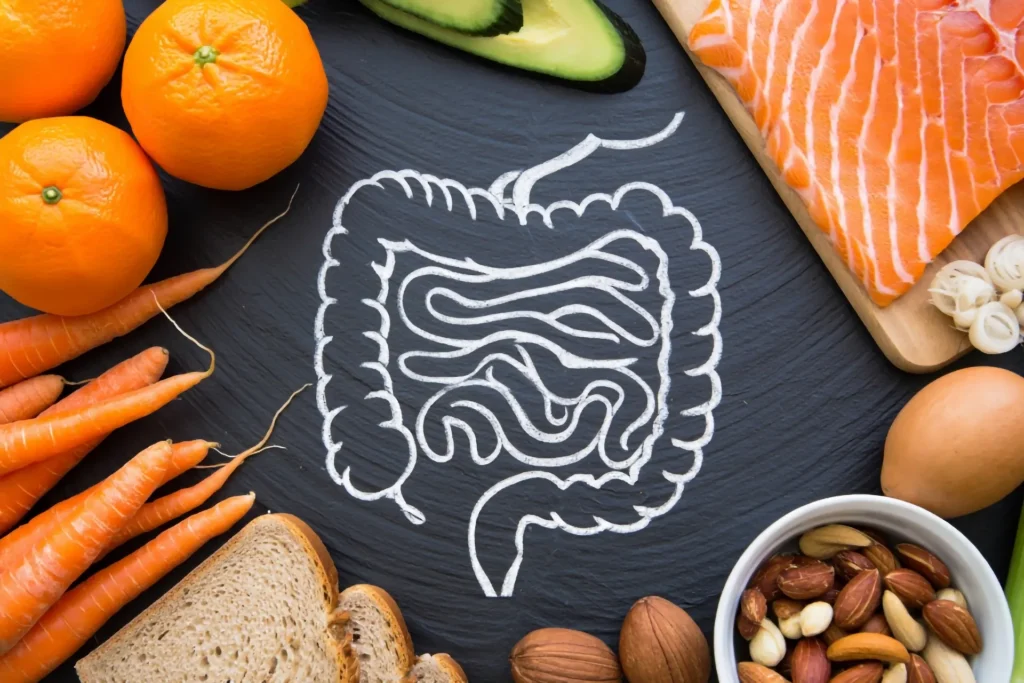 Un intestino disegnato su una lavagna e intorno ad esso delle arance, salmone, carote, pane e frutta secca