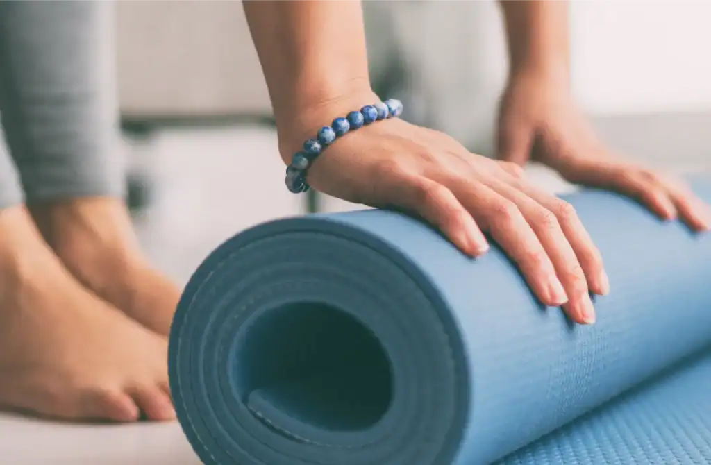 Persona che fa esercizi di yoga con tappetino blu in casa.